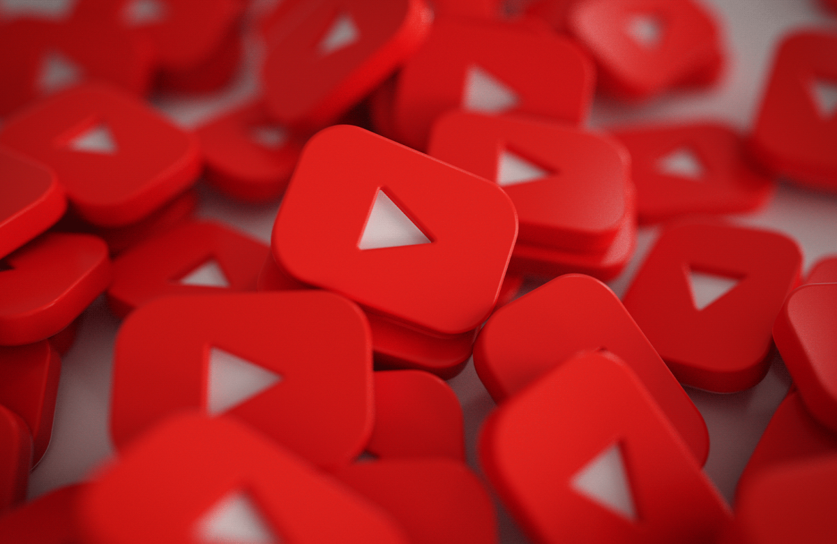 Крупный план нескольких красных значков кнопок воспроизведения YouTube, разбросанных в произвольном порядке, что создает динамичную и визуально привлекательную композицию