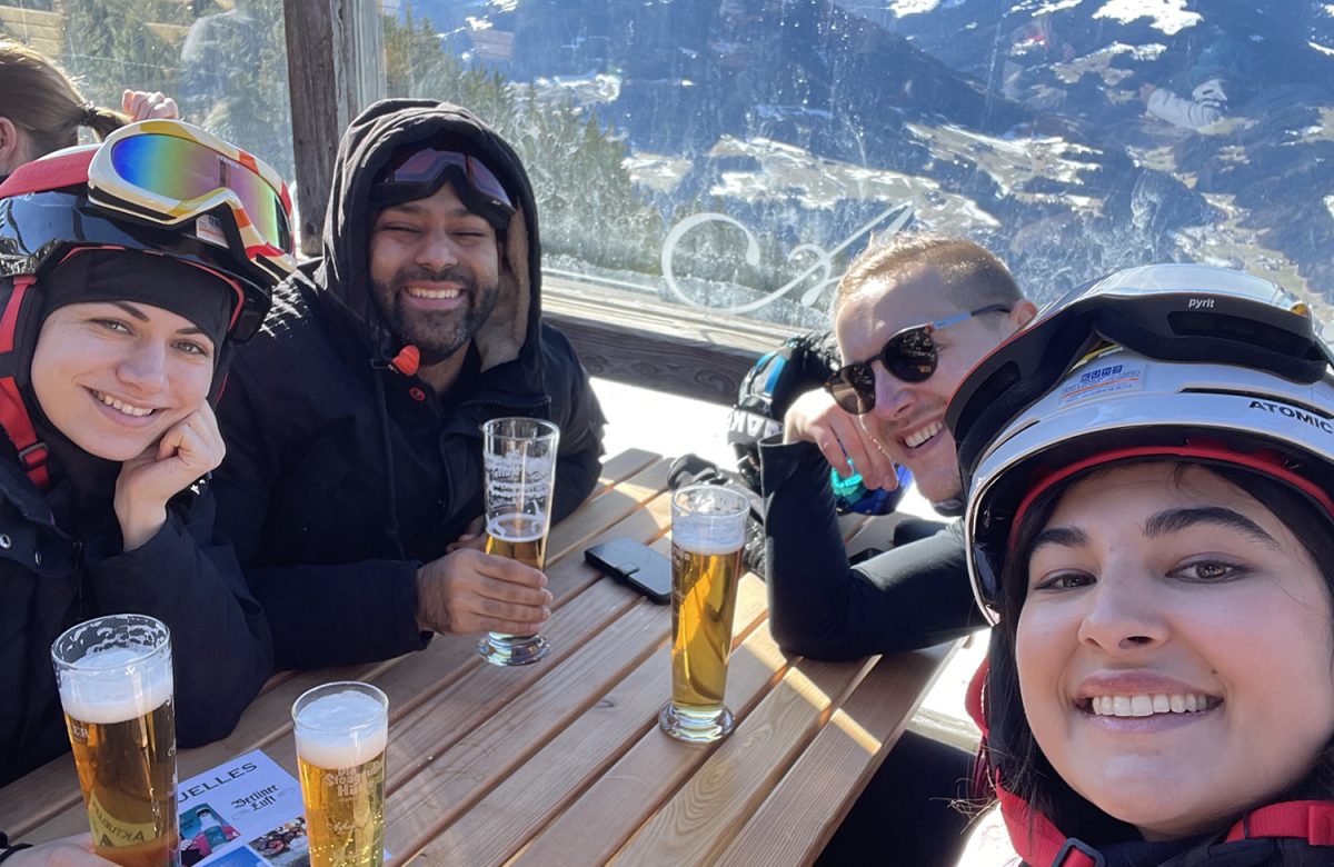 A group enjoying drinks and laughter after a long day of skiing, sitting at an outdoor wooden table