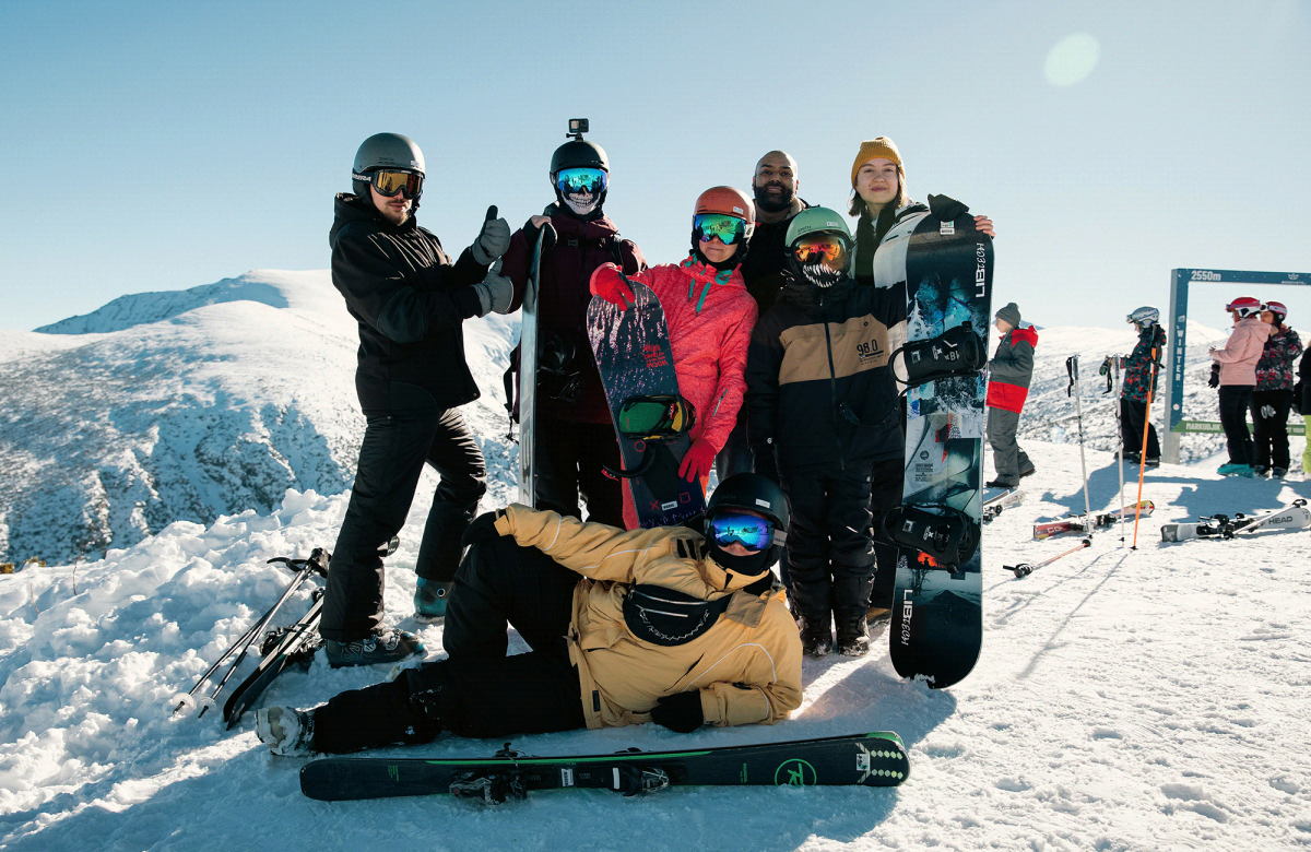 A group of snowboarders posing with their gear on top of a snowy mountain