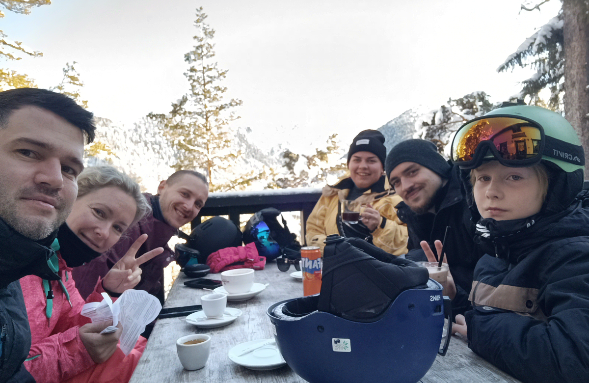 A group of friends enjoying breakfast in a snowy mountain setting, with warm drinks and food on the table
